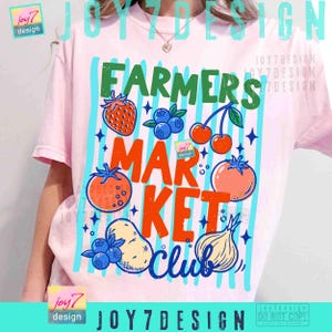 May include: A light pink t-shirt with a colorful graphic design. The design features the words "FARMERS MARKET CLUB" with illustrations of fruits and vegetables, including a strawberry, blueberries, cherries, and tomatoes.