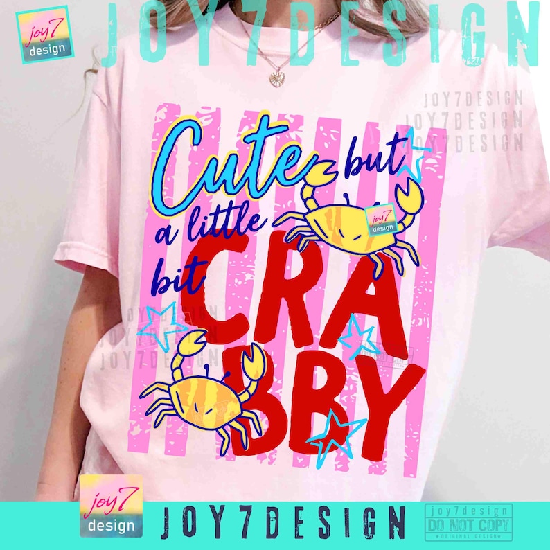 May include: Pink t-shirt with a graphic design featuring the text "Cute but a little bit Crabby" in blue, red, and yellow. The design includes two yellow crab illustrations and blue star accents.