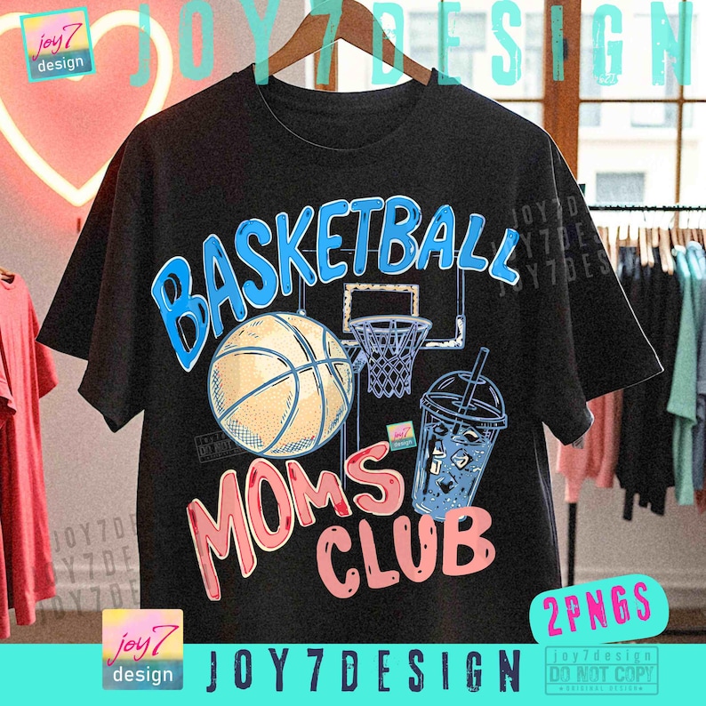 May include: Black t-shirt with a basketball graphic. The design includes a basketball, hoop, and a drink, with the words "BASKETBALL MOMS CLUB" in blue and pink. The shirt is hanging on a wooden hanger.