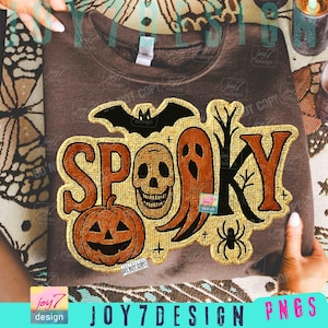 May include: A brown sweatshirt with a gold and orange "Spooky" design. The design includes a bat, skull, ghost, pumpkin, tree, and spider. The text "JOY7DESIGN PNGS" is at the bottom.