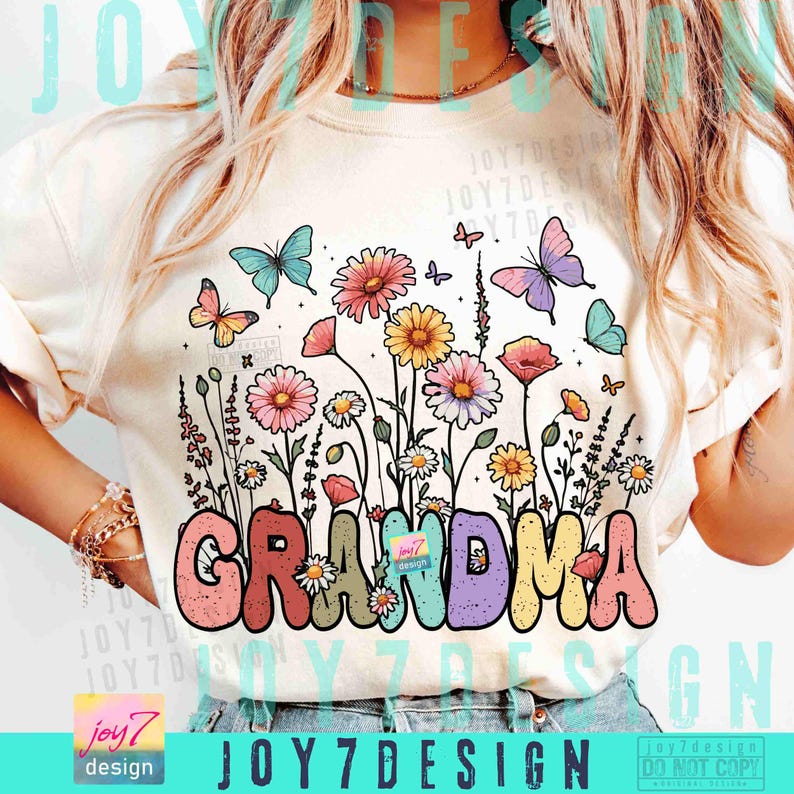 May include: Cream-colored t-shirt featuring a colorful floral design with butterflies and the word "GRANDMA" in a bubble font. The design includes pink, yellow, and blue flowers, with butterflies in shades of blue, pink, and orange.