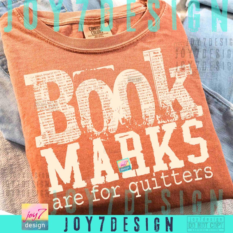 May include: An orange Comfort Colors t-shirt with the text "Book Marks are for quitters" in a distressed white font. The shirt is folded and appears to be made of soft material. The design includes the Joy7Design logo.
