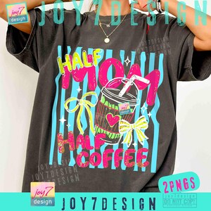 May include: Dark gray t-shirt with the text "HALF MOM HALF COFFEE" in pink and yellow. The design includes a coffee cup with a heart and bows, set against blue vertical stripes. The shirt has a vintage look.