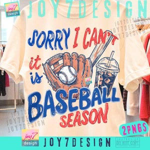 May include: Cream-colored t-shirt with a baseball-themed graphic. The design includes a baseball, mitt, bat, and a drink with a straw. Text reads "Sorry I can't, it is Baseball Season" in blue and red.