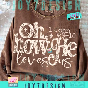 May include: Brown sweatshirt with the text "Oh how He loves us" in a decorative font. The text includes floral and cross designs. The phrase "1 John 4:9-10" is also printed on the shirt. A gold chain is draped across the top.