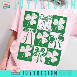 Puede incluir: Camiseta rosa claro con un dise&ntilde;o verde y blanco de tr&eacute;boles y lazos en un patr&oacute;n de cuadr&iacute;cula. El texto "JOY7 DESIGN" est&aacute; impreso en la parte inferior. El dise&ntilde;o tiene un aspecto vintage.