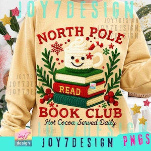 Może przedstawiać: Beżowa bluza z świątecznym wzorem. Wzór zawiera napisy "NORTH POLE BOOK CLUB" ze stosem książek i uśmiechniętym kubkiem kakao. Tekst "Hot Cocoa Served Daily" jest również zawarty.