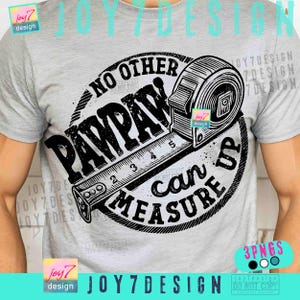 May include: A light gray t-shirt with a black graphic design. The design features a tape measure with the words "PAWPAW" and "NO OTHER CAN MEASURE UP" in a circular arrangement. The shirt is a crew neck.