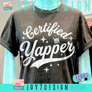 Könnte beinhalten: Dunkelgraues T-Shirt mit dem Schriftzug "Certified Yapper" in verblichener weißer Schrift und Sternen. Das Design beinhaltet das Logo "joy7 design". Die Ärmel sind hochgekrempelt.