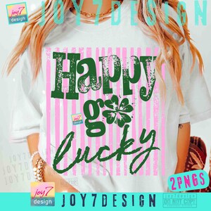 Może przedstawiać: Biała koszulka z napisem "Happy go Lucky" w kolorze zielonym, z grafiką czterolistnej koniczyny. Projekt umieszczono na r&oacute;żowym tle w paski. Koszulka ma swobodny, luźny kr&oacute;j.