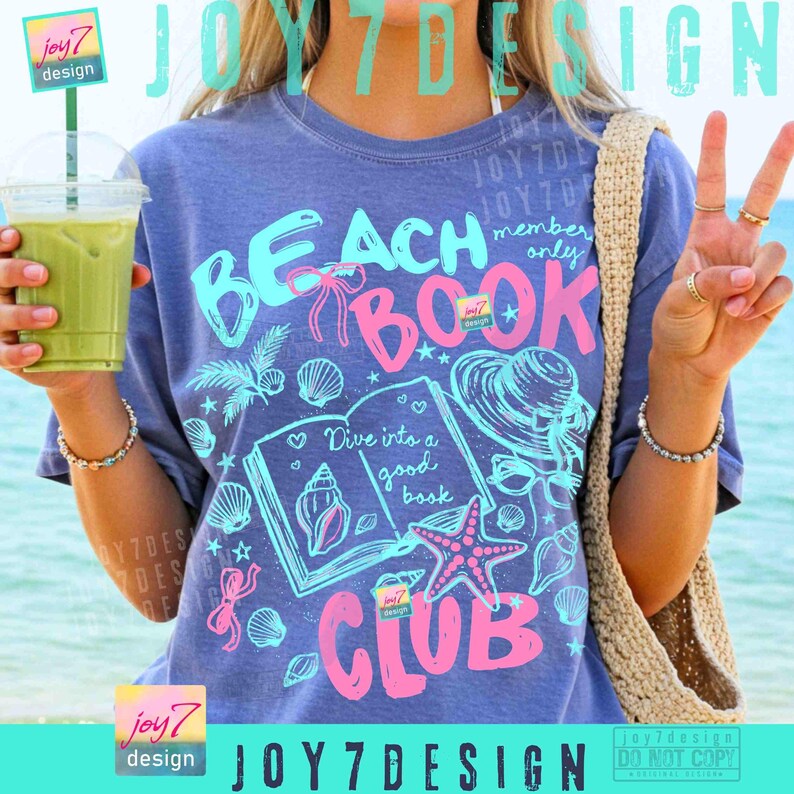 May include: A blue t-shirt with the words "BEACH BOOK CLUB" in pink and turquoise. The shirt features a graphic of a book, seashells, and a starfish. The text "Dive into a good book" is also visible. The shirt is part of the "JOY7 DESIGN" collection.