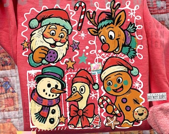 May include: Red sweatshirt with a festive Christmas design. The graphic features Santa Claus, a reindeer, a snowman, a duck, and a gingerbread man, all wearing Santa hats. The text "JOY7DESIGN 2PNGS" is at the bottom.