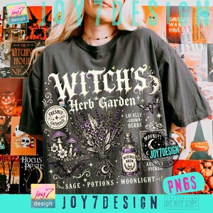 May include: A dark gray t-shirt featuring a graphic print with the text "WITCH'S Herb Garden". The design includes illustrations of a lavender bouquet, mushrooms, a bat, a moth, and a glass bottle labeled "WITCHES BREW" with stars and moon motifs.