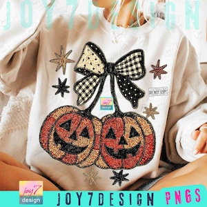 以下が含まれることがあります： ハロウィーンのデザインが施された白いスウェットシャツ。デザインには、黒いジャック・オー・ランタンの顔が付いた2つのオレンジ色のカボチャ、白と黒のチェック柄のリボン、星のアクセントが含まれています。「JOY7DESIGN PNGS」というテキストが下にあります。