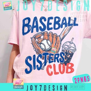 May include: Pink t-shirt with a baseball-themed graphic. The design includes a baseball, mitt, bat, and a drink, with the words "BASEBALL SISTERS CLUB" in blue and red. The shirt also has the text "2PNGS".