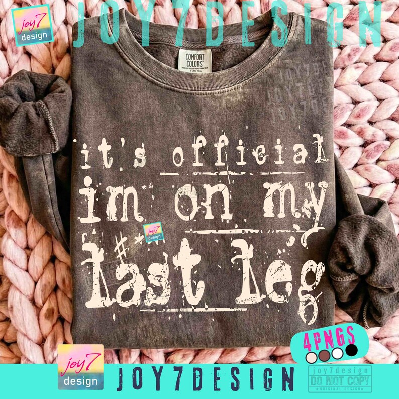 May include: A dark gray sweatshirt with the text "it's official I'm on my last leg" in white lettering. The sweatshirt has a crew neck and long sleeves. The brand name "JOY7DESIGN" is visible in the image.