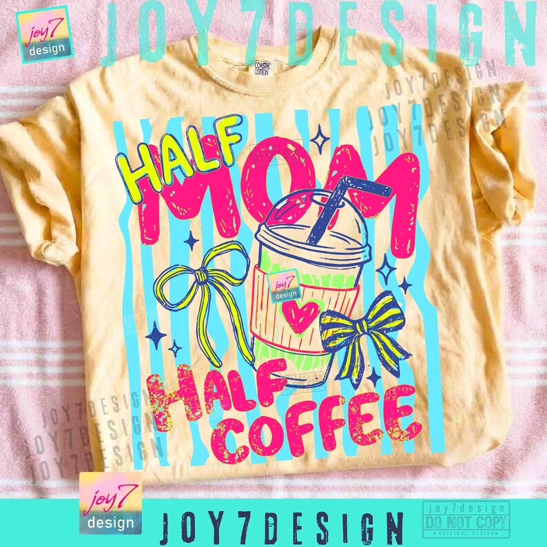 May include: A light yellow t-shirt with a colorful graphic design. The design features the words "HALF MOM HALF COFFEE" in bright pink and yellow, along with a cartoon coffee cup and bows. The shirt has a crew neck and short sleeves.