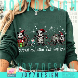 Puede incluir: Sudadera verde oscuro con un dise&ntilde;o festivo. Presenta tres zarig&uuml;eyas con gorros de Pap&aacute; Noel y luces navide&ntilde;as. El texto "overstimulated but festive" est&aacute; impreso debajo. El dise&ntilde;o incluye copos de nieve y estrellas.