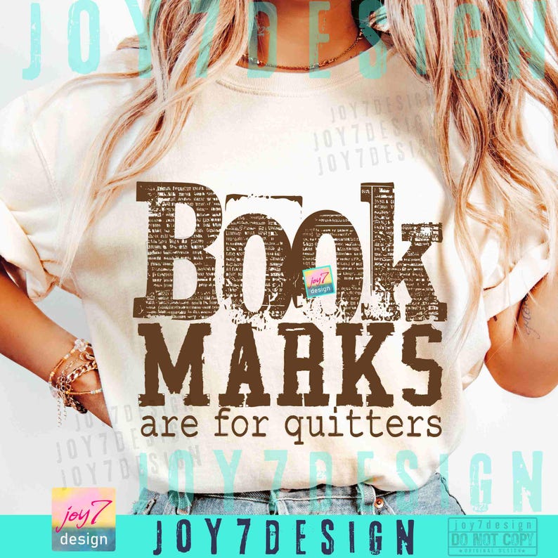 May include: Cream-colored t-shirt with the text "Book Marks are for quitters" in brown, distressed lettering. The shirt features a small logo and the brand name "JOY7DESIGN" at the bottom. The shirt is a casual wear item.