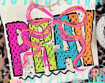 May include: Cream-colored t-shirt with the word "PRAY" in large, colorful letters. The letters are outlined in black and filled with neon green, blue, and orange. A large, pink and orange bow is above the word. A gold necklace is at the top.