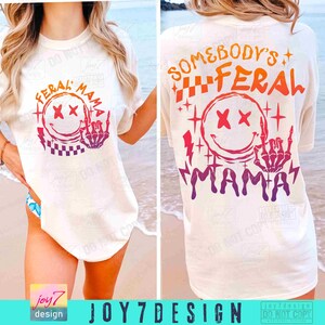K&ouml;nnte beinhalten: Ein wei&szlig;es T-Shirt mit einem bunten Grafikdesign, das ein Smiley-Gesicht mit gekreuzten Augen und eine Skeletthand zeigt, die den Mittelfinger zeigt. Der Text "Feral Mama" steht &uuml;ber dem Smiley-Gesicht und der Text "Somebody's Feral Mama" steht unter dem Smiley-Gesicht.