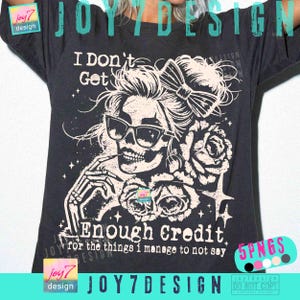 May include: Dark grey t-shirt featuring a white graphic of a skull wearing sunglasses and a bow, holding a cigarette. Text reads "I Don't Get Enough Credit for the things I manage to not say." The design includes roses and stars.