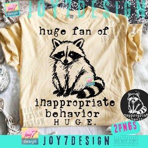 May include: A light yellow t-shirt featuring a black and white raccoon illustration. The text "huge fan of inappropriate behavior HUGE" is printed below the raccoon. A small circular graphic of the raccoon is on the right.