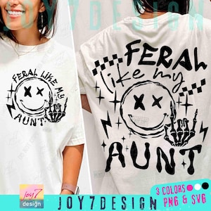 以下が含まれることがあります： 黒いグラフィックデザインの白いTシャツ。デザインは、目がバツになったスマイリーフェイス、中指を立てている骸骨の手、そして「FERAL like my AUNT」というテキストが特徴です。シャツはクルーネックです。