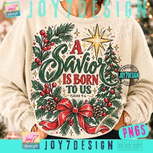 Op de afbeelding: Een crèmekleurig sweatshirt met ronde hals en een feestelijke afbeelding van een dennenkrans met rode bessen, dennenappels en een grote rode strik. De tekst luidt A SAVIOR IS BORN TO US ISAIAH 9:6 onder een gouden ster.