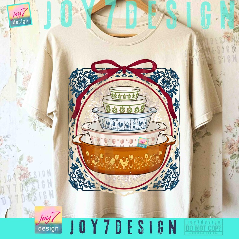 May include: A beige t-shirt featuring a graphic of a stack of vintage casserole dishes in various colors and patterns. The design is framed by a red ribbon and a blue and white floral border. The text "JOY7DESIGN" is visible.