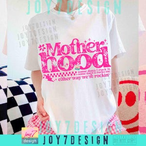Peut inclure: T-shirt blanc avec un motif rose "Motherhood" dans une police d&eacute;corative. Le motif comprend des &eacute;l&eacute;ments floraux et le texte "some days I rock it, some days it rocks me, either way we're rockin'".