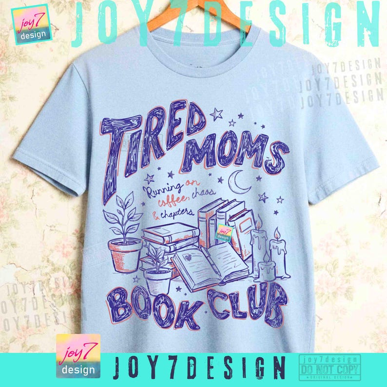 May include: Pale blue t-shirt featuring the text "Tired Moms Book Club" in a playful font. The design incorporates illustrations of books, candles, plants, and stars. The phrase "Running on coffee, chaos & chapters" is also included.