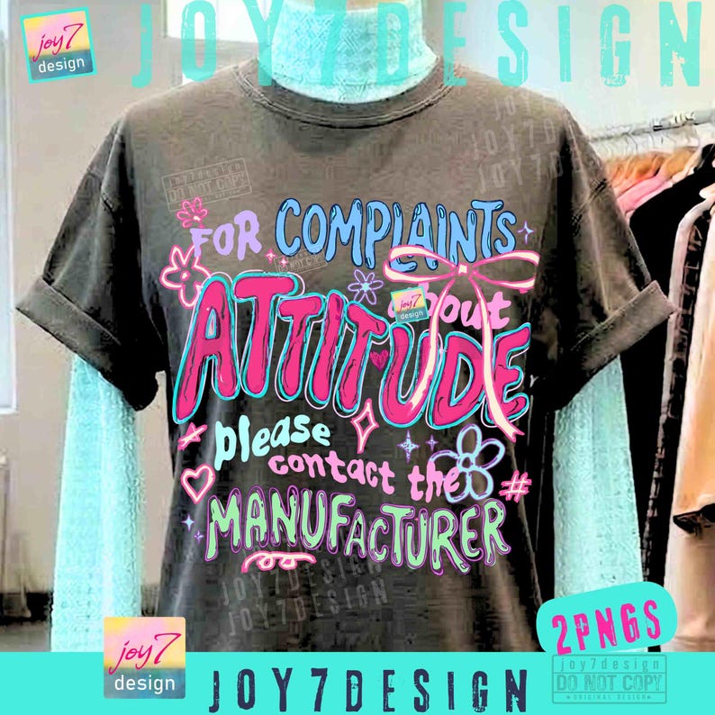 May include: Dark gray t-shirt with the text "FOR COMPLAINTS ABOUT ATTITUDE please contact the MANUFACTURER" in pink, blue, and green. The shirt has rolled-up sleeves and is layered over a light blue turtleneck. The design includes floral and bow accents.