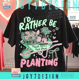 May include: Black t-shirt with a gardening-themed graphic. The design features a wheelbarrow filled with flowers, a small tree, and the text "I'd Rather Be Planting." The text "Plants Don't Talk Back" is also included.