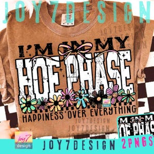 May include: Brown long-sleeve shirt with the text "I'M IN MY HOE PHASE" in a distressed white font. The shirt features a floral design at the bottom with the words "HAPPINESS OVER EVERYTHING".