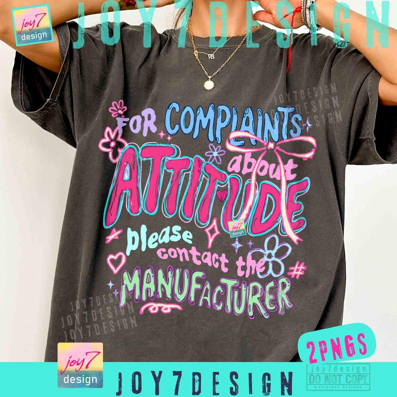 May include: Dark gray t-shirt with the text "FOR COMPLAINTS about ATTITUDE please contact the MANUFACTURER" in pink, blue, and white. The design includes flowers, hearts, and a bow. The brand name "joy7 design" is also visible.