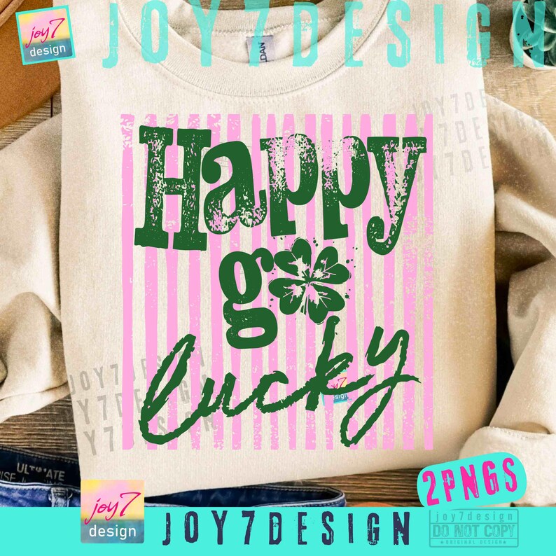 Może przedstawiać: Beżowa bluza z napisem "Happy go lucky" w kolorze zielonym, z r&oacute;żowym paskowanym tłem i zieloną koniczyną. Bluza ma r&oacute;wnież tekst "joy7 design" w lewym dolnym rogu.