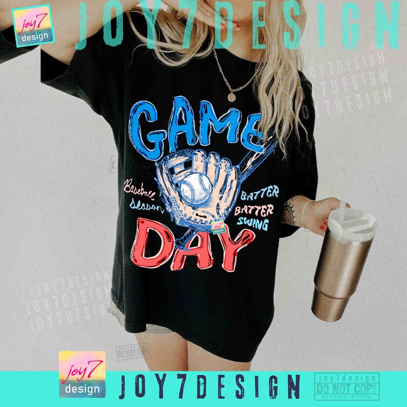 May include: Black t-shirt with a baseball-themed graphic. The design features the word "GAME" in blue, "DAY" in red, and a baseball glove with a ball. Additional text includes "Baseball Season", "Batter, Batter, Swing".