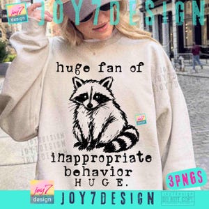May include: A beige sweatshirt with a black and white raccoon illustration. The text reads "huge fan of inappropriate behavior HUGE." The design includes the "joy7 design" logo and "3PNGS" text.