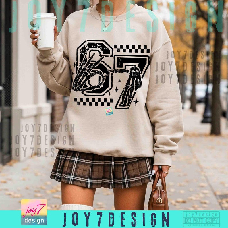 Peut inclure: Sweat-shirt beige avec un motif noir et blanc du chiffre 67, orn&eacute; de mains de squelette et d'un motif &agrave; carreaux. La tenue comprend une jupe pliss&eacute;e &agrave; carreaux marron. Un petit sac &agrave; main marron et une tasse de caf&eacute; sont &eacute;galement visibles.