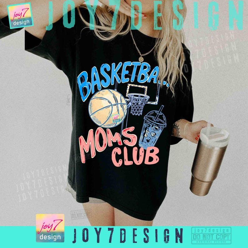 May include: Black t-shirt with a basketball-themed graphic. The design features a basketball, hoop, and a drink, with the words "BASKETBALL MOMS CLUB" in blue and pink. The shirt is a casual style.