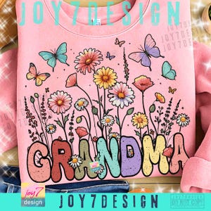 May include: Pink sweatshirt with a floral design and the word "GRANDMA" in colorful bubble letters. The design includes butterflies and various flowers in shades of pink, yellow, and blue. The text "JOY7DESIGN" is also visible.