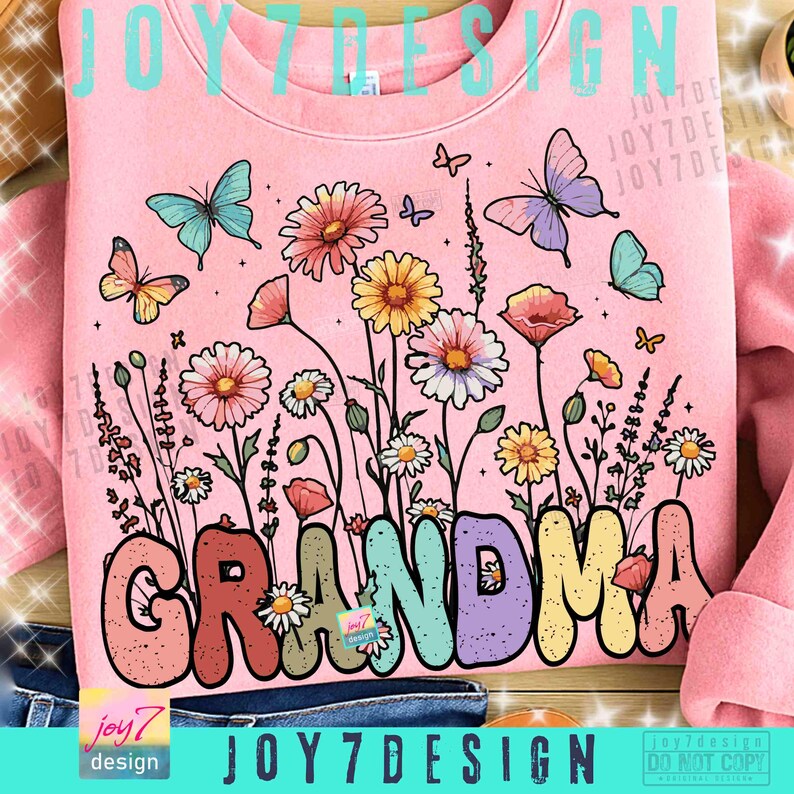 May include: Pink sweatshirt with a floral design and the word "GRANDMA" in colorful bubble letters. The design includes butterflies and various flowers in shades of pink, yellow, and blue. The text "JOY7DESIGN" is also visible.
