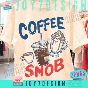May include: Cream-colored t-shirt with a graphic design featuring the word "COFFEE" in blue, and "SNOB" in red. The design includes illustrations of coffee drinks: a small cup, a to-go cup with ice, and a whipped cream-topped beverage.