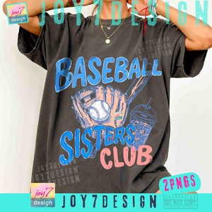 May include: Dark gray t-shirt with a baseball-themed graphic. The design features the word "BASEBALL" in blue, a baseball glove, a baseball, and the words "SISTERS CLUB" in blue and pink. A drink is also included in the design.