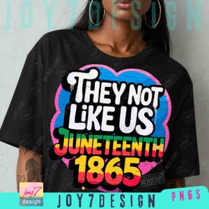 Op de afbeelding: Zwart T-shirt met een kleurrijk grafisch ontwerp. Het ontwerp toont de tekst "THEY NOT LIKE US" in wit, "JUNETEENTH" in groen, geel en rood en "1865" in geel en rood. Het ontwerp staat op een hartvormige achtergrond.