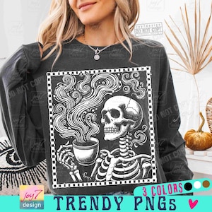 May include: Dark gray sweatshirt featuring a black and white graphic of a skeleton drinking from a coffee cup. The design includes the text "TRENDY PNGS" and "3 COLORS".