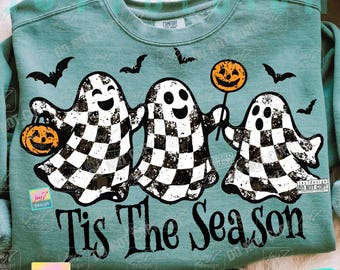 May include: A teal sweatshirt featuring a Halloween design. Three ghosts with checkered patterns are holding a pumpkin and a pumpkin lollipop. The phrase "Tis The Season" is printed below the ghosts, with bats flying above.