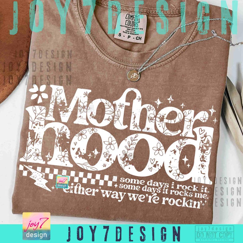 Peut inclure: Un t-shirt marron avec le mot "Motherhood" en grandes lettres blanches, orn&eacute; de motifs floraux et d'&eacute;toiles. Le t-shirt comporte &eacute;galement le texte "some days I rock it, some days it rocks me, either way we're rockin'". Un collier argent&eacute; avec un pendentif est pos&eacute; sur le t-shirt.