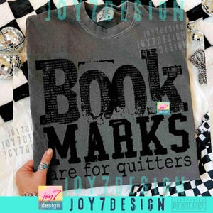 May include: A gray t-shirt with the words "BOOK MARKS are for quitters" in black. The word "BOOK" is large and stylized. The shirt has a crew neck and short sleeves. The shirt is a medium size.